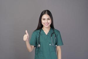 Eine Ärztin, die ein grünes Peeling und ein Stethoskop trägt, befindet sich auf einem grauen Hintergrundstudio