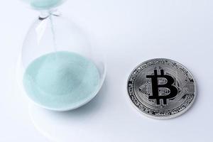 Silber Bitcoin und Sanduhr auf weißem Hintergrund. foto