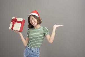 Porträt einer schönen Frau mit rotem Weihnachtsmann-Hut, die Geschenkbox über Studiohintergrund, Weihnachten und Neujahrskonzept hält foto