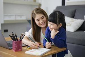 Asiatische glückliche Mutter und Tochter verwenden Laptop zum Online-Lernen über das Internet zu Hause. E-Learning-Konzept während der Quarantänezeit. foto