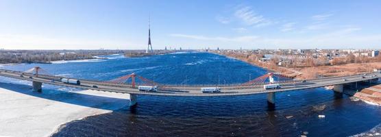 Luftaufnahme der Südbrücke über den Fluss Daugava in Lettland mit einem Eis geformten Mustern, die im Fluss schwimmen.