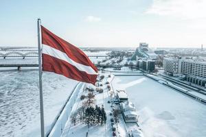 Panorama der Stadt Riga mit einer großen lettischen Flagge im Vordergrund während des sonnigen Wintertages. foto