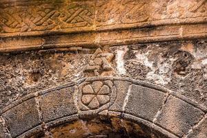 Nahaufnahme des traditionellen Schnitzens an der alten verwitterten Steinmauer? foto