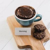 Tasse Kaffee mit dunklen Schokoladenkeksen und Grußbotschaft auf Holzplatte im Café foto