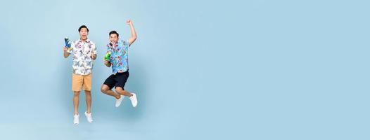 lächeln glückliche asiatische männliche Freunde, die mit Wasserpistolen spielen und auf blauem Bannerhintergrund mit Kopienraum für das Songkran-Festival in Thailand und Südostasien springen foto