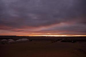 Touristenzelte auf Sand in der Wüste gegen bewölktem Himmel während der Dämmerung foto