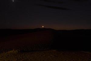 Wüstenlandschaft mit Mond und Sternen über Sanddünen während der Nacht foto