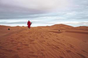 Mann in traditioneller Kleidung mit Sandbrett, der auf Sanddünen gegen Himmel steht foto