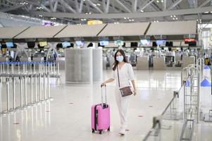 Eine reisende Frau trägt eine Schutzmaske auf dem internationalen Flughafen, reist unter der Covid-19-Pandemie, Sicherheitsreisen, Protokoll zur sozialen Distanzierung, neues normales Reisekonzept foto