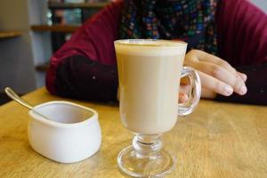 eine Tasse späten Kaffee im Café auf dem Tisch, während eine Frau auf einem Stuhl sitzt foto
