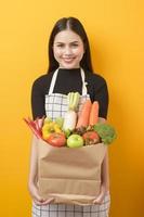 schöne junge Frau hält Gemüse in der Einkaufstüte im gelben Studiohintergrund