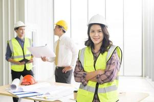 Porträt einer selbstbewussten Ingenieurin, die auf der Fassade steht, während Kollegen über den Hintergrund diskutieren und sich treffen foto