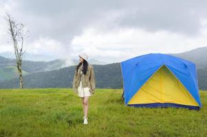 Fröhliche reisende Frau, die in der Regenzeit, tropisches Klima, in der Nähe des Campzeltes über einem schönen grünen Berg genießt und sich entspannt. foto