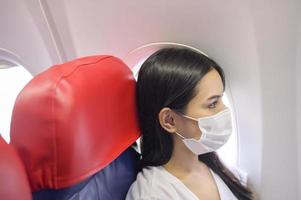 Die reisende Frau trägt eine Schutzmaske an Bord im Flugzeug, reist unter der Covid-19-Pandemie, Sicherheitsreisen, Protokoll zur sozialen Distanzierung, neues normales Reisekonzept foto