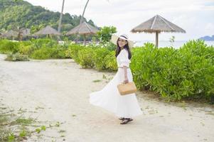 eine glückliche schöne Frau im weißen Kleid, die am Strand, im Sommer und im Ferienkonzept genießt und sich entspannt foto