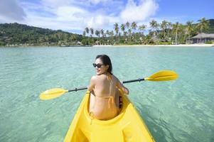 junge sportliche Frau, die an einem sonnigen Tag am Meer Kajak fährt foto