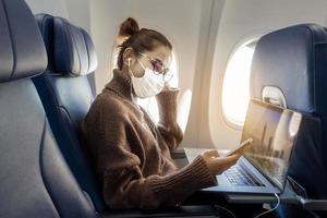 Eine junge Frau mit Gesichtsmaske reist im Flugzeug, neue normale Reise nach dem Konzept der Covid-19-Pandemie foto