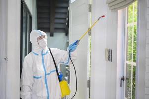 Ein medizinisches Personal im PSA-Anzug verwendet Desinfektionsspray im Wohnzimmer, Covid-19-Schutz, Desinfektionskonzept. foto