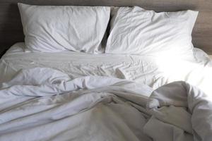 weißes kissen und decke auf dem bett ungemacht. Unordentliches Bett nach Gebrauch. zerknittertes weißes Bett, Kissen und Bettlaken foto