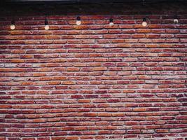 Rote Backsteinmauer mit Glühbirnen Vintage und Retro-Hintergrund. Leere Wand aus rotem Backstein mit Glühbirnenhintergrund. Dekoration im industriellen Loft-Stil. foto