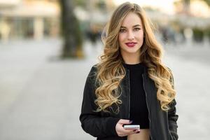blonde Frau SMS mit ihrem Smartphone im städtischen Hintergrund foto