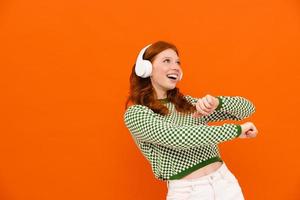 glückliche ingwerfrau im karierten pullover, der mit kopfhörern tanzt foto