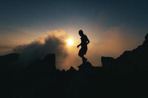 Ein Mann in Silhouette geht während einer einsamen Meditation über einen felsigen Grat foto