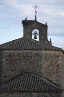 Alte ländliche Kirche in Spanien aus Stein. Turm mit einer Glocke, einem metallischen Windmesser und einem Storch in seinem Nest foto