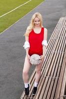 Fußballspielerin steht mit dem Ball auf der Bank in Rot. foto