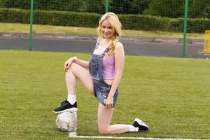 Blondes Mädchen mit einem Ball, der auf einem Fußballfeld sitzt. foto