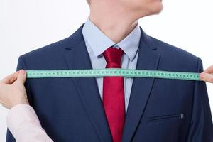 Nahaufnahmebild des Schneiders, der Maße für Geschäftsjackenanzug nimmt. Geschäftsmann in roter Krawatte und blauem Anzug im Studio isoliert auf weißem Hintergrund. foto