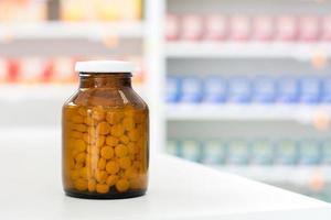 kleine Pillen in transparenter bernsteinfarbener Medizinflasche am Tisch in der Apotheke foto