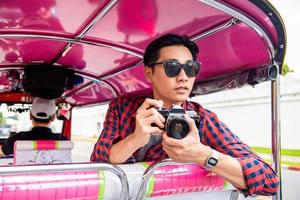 hübscher männlicher asiatischer tourist, der kamera auf tuk-tuk-taxi in bangkok thailand während der sommerferien alleinreisend hält foto