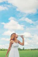 Frauen-Lifestyle-Konzept junge schöne Frau mit weißem Kleid Trinkwasser im grünen Sommerpark. foto