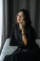 Frau trägt ein weißes Hemd, sitzt auf dem Bett und telefoniert. foto