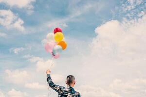 Der Rücken eines glücklichen jungen Hipster-Mannes, der bunte Luftballons in der Wiese hält, genießt das Leben und ist glücklich. foto