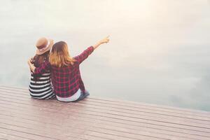 freundschaft, zwei frauen sitzen auf dem pier, entspannen sich und verbringen gute zeit miteinander. foto