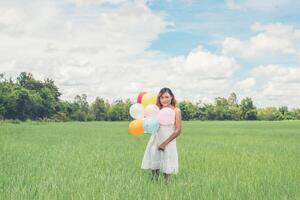 glückliche junge schöne frau, die luftballons auf der wiese hält, genießen sie mit frischer luft. foto