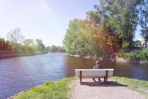 ein junger Mann, der auf einer Bank in der Nähe des Flusses sitzt. foto