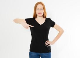 T-Shirt-Design, Konzept der glücklichen Menschen - lächelnde Frau mit roten Haaren in leerem schwarzem T-Shirt, die ihre Finger auf sich selbst zeigt, T-Shirt-Attrappe für Mädchen mit rotem Kopf foto