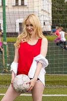 die Blondine in roter Form mit einem Ball am Tor auf dem Fußballplatz. foto