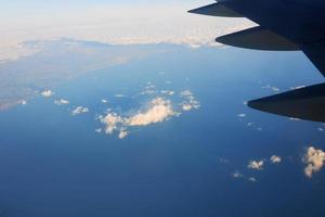 blick auf den flügel des flugzeugs in den himmel und das meer. Reise- und Transportkonzept foto