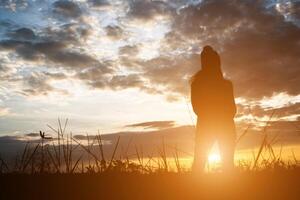 Silhouette einer Frau, die während des Sonnenuntergangs auf dem Feld steht. foto