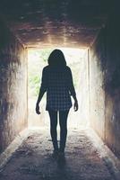 Silhouette einer Hipster-Frau, die im Tunnel spazieren geht. Licht am Ende des Tunnels foto