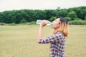 Junge Hipster-Frau trinkt Wasser im grünen Sommerpark. foto