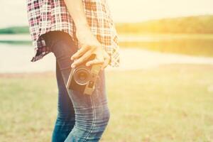 Junge schöne Hipster-Frau, die draußen eine Retro-Kamera mit der Natur hält, genießt die frische Luft. foto