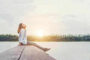 junge schöne hipster-frau, die auf dem see sitzt und sich an der frischen luft entspannt. foto