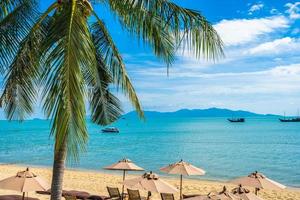 schönes tropisches Strandmeer und -ozean mit Kokosnusspalme und -schirm und -stuhl auf blauem Himmel und weißer Wolke