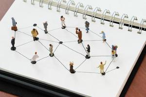 Nahaufnahme von Miniaturmenschen mit sozialem Netzwerkdiagramm auf offenem Notizbuch auf Holzschreibtisch als Social-Media-Konzept foto