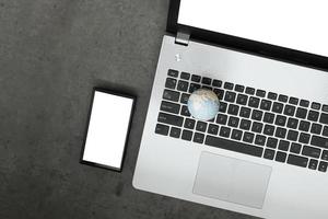 Handgezeichnete Textur-Globus mit Laptop-Computer mit leerem Bildschirm und Smartphone als Internet-Konzept auf Zement-Textur-Tischhintergrund foto